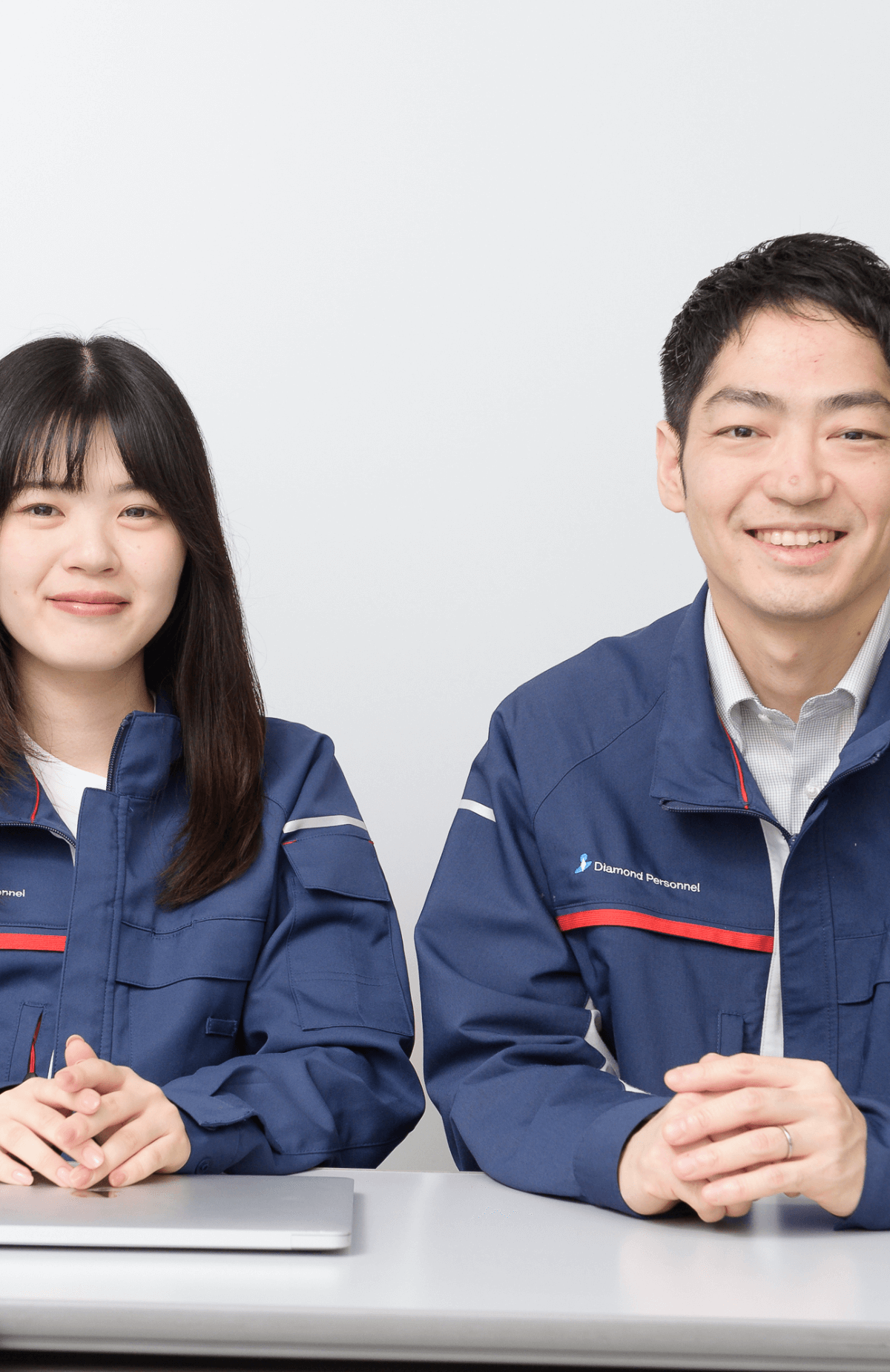 青い作業服を着た男女がテーブルに座り、笑顔で前を向いている